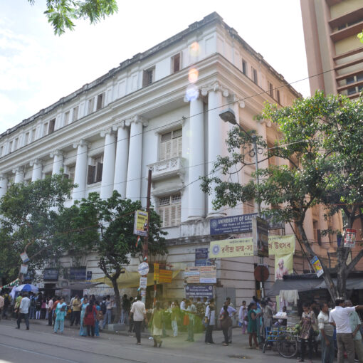 University of Calcutta building photographed from across the street, with name of university on sign in corner of building. Crowded street can be seen in foreground.